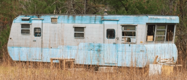 Older mobile home sitting abandoned in an overgrown field